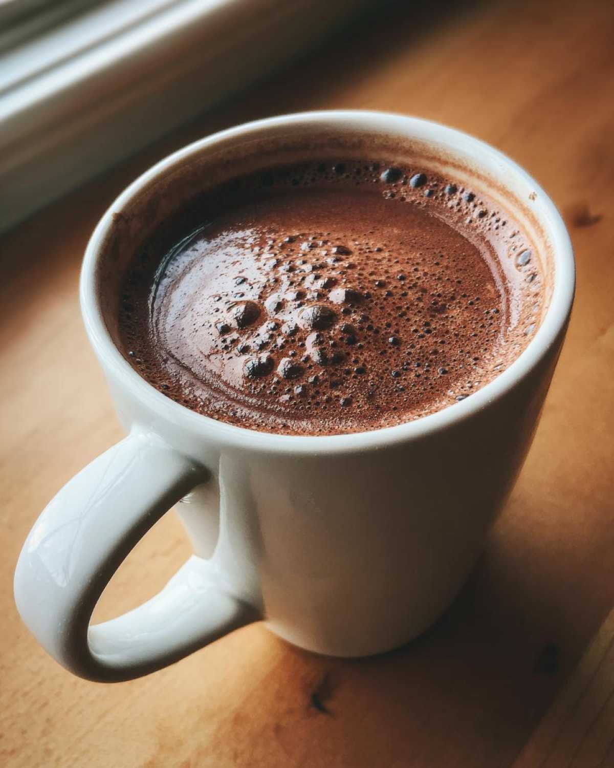 Close-up of a white mug filled with rich, dark hot cocoa mix, showing a foamy top.