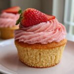 A close-up of one perfectly baked strawberry cupcake topped with pink frosting and a fresh strawberry slice.