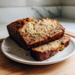 Close-up of a loaf of moist sugar free banana bread, with two thick slices cut and resting on a white plate.