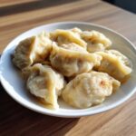 A white bowl filled with freshly steamed Traditional Chinese Dumplings resting on a wooden table.