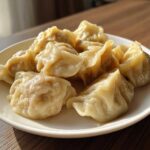 A close-up of several freshly steamed Traditional Chinese Dumplings piled on a white plate, glistening under natural light.