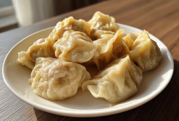A close-up of several freshly steamed Traditional Chinese Dumplings piled on a white plate, glistening under natural light.