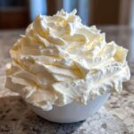 A close-up of fluffy, perfectly piped vanilla buttercream frosting piled high in a small white bowl.