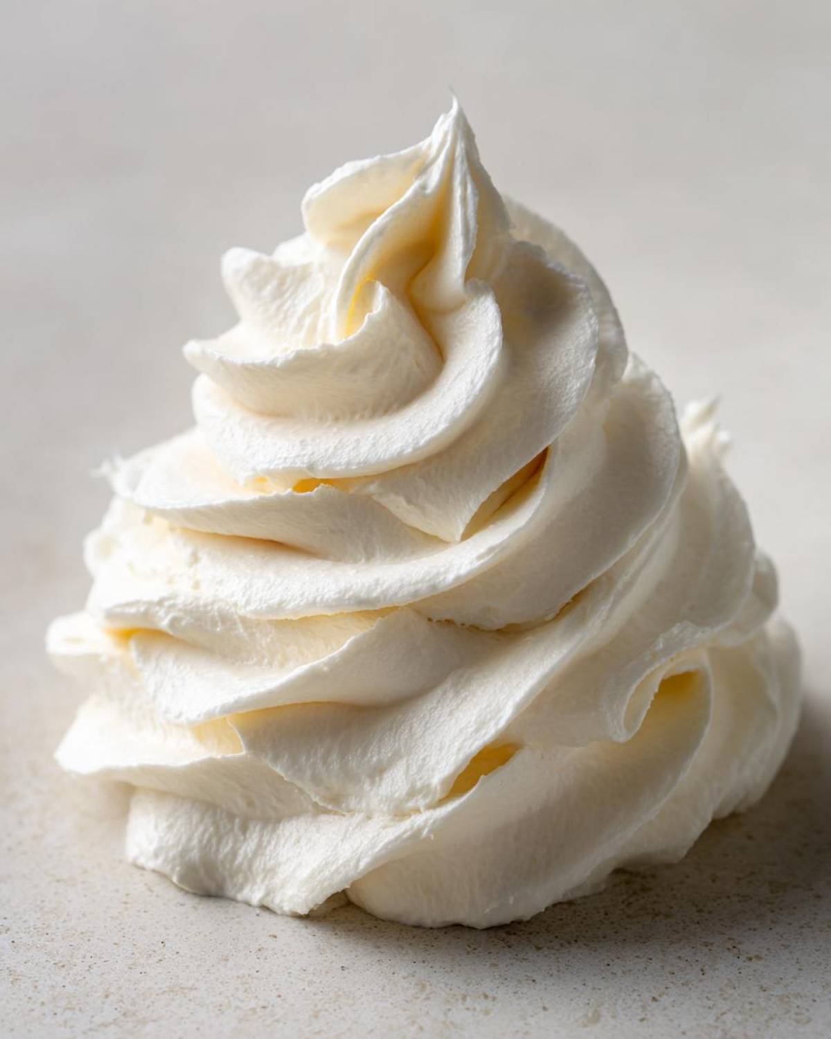 Close-up of a perfectly piped swirl of creamy vanilla buttercream frosting on a light surface.