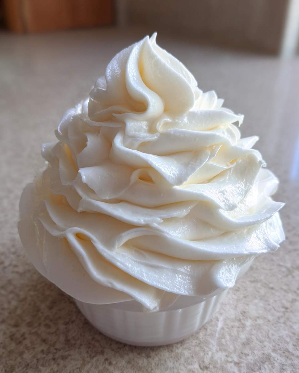 Close-up of a perfectly piped swirl of creamy white vanilla buttercream frosting in a small dish.