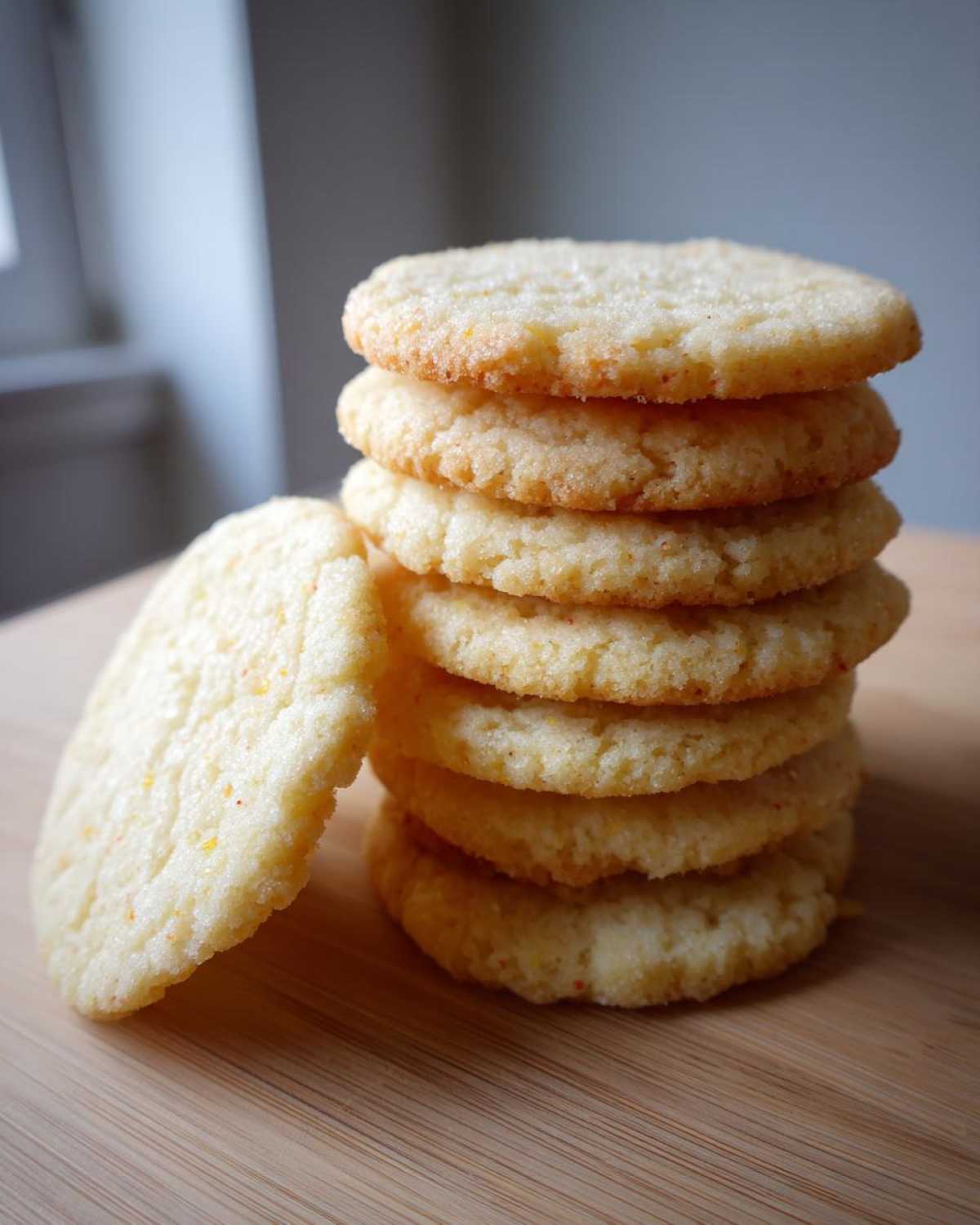 A tall stack of golden brown vegan sugar cookies resting on a wooden cutting board.