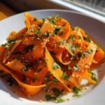 Close-up of a vibrant raw carrot salad made with shaved carrot ribbons, topped with fresh parsley and sesame seeds.