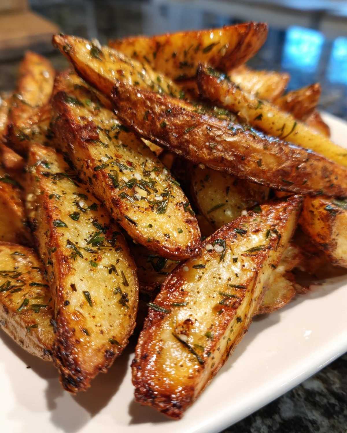 A close-up of golden brown Air Fryer Crispy Rosemary Potato Wedges seasoned with herbs and salt.
