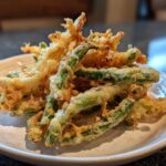Close-up of golden, crispy Air Fryer Crispy Tempura Green Beans piled on a small white plate.