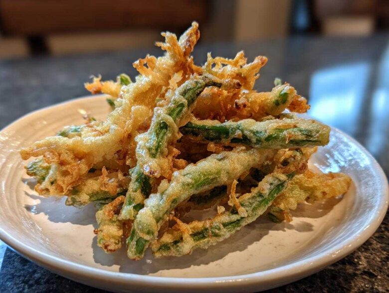 Close-up of golden, crispy Air Fryer Crispy Tempura Green Beans piled on a small white plate.