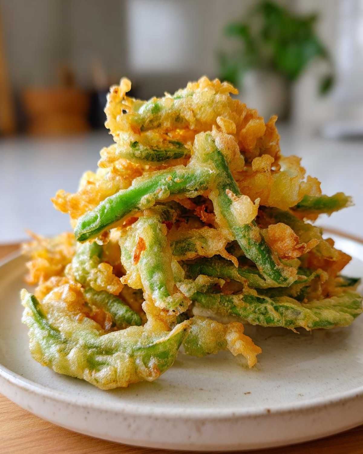 A mound of golden, crispy Air Fryer Crispy Tempura Green Beans piled high on a light ceramic plate.