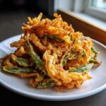 A close-up of a pile of golden brown Air Fryer Crispy Tempura Green Beans served on a white plate.