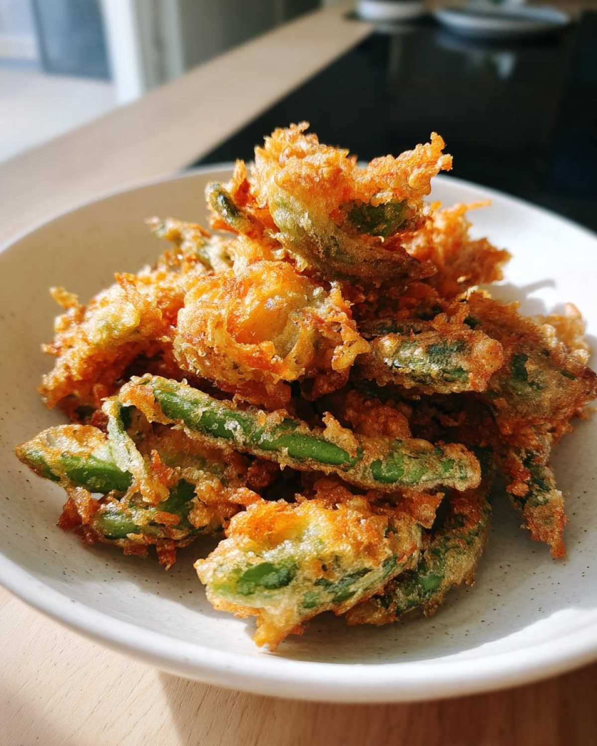 A close-up of golden, crispy Air Fryer Crispy Tempura Green Beans piled high in a speckled white bowl.