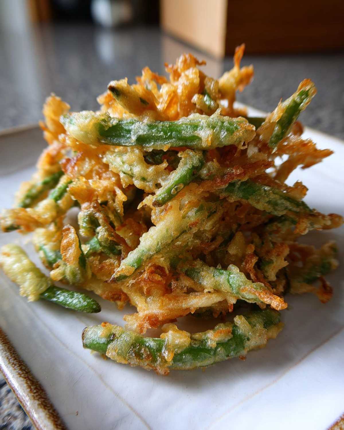 A pile of golden brown, crispy Air Fryer Crispy Tempura Green Beans stacked on a white square plate.