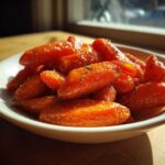 A close-up of glossy Air Fryer Maple Glazed Carrots piled in a white bowl, seasoned with herbs.