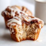 Close-up of a Gluten-Free Cinnamon Roll Muffin with a bite taken out, showing the soft interior and white icing drizzle.