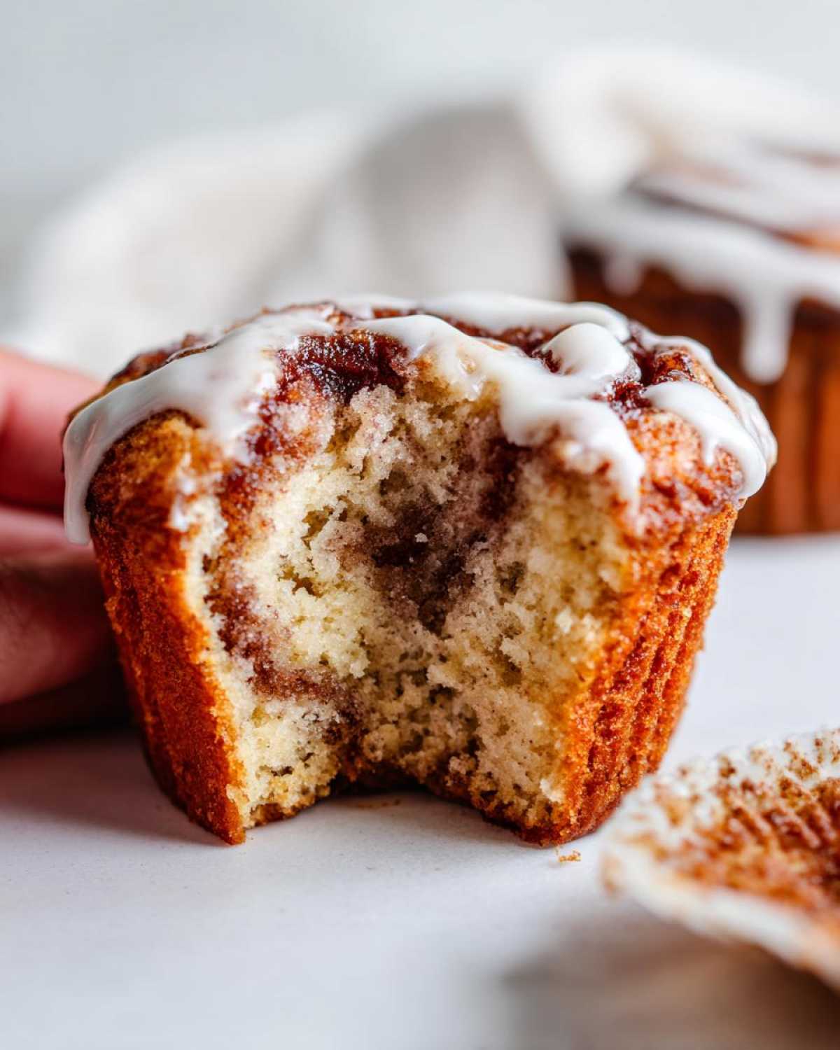 Close-up of a Gluten-Free Cinnamon Roll Muffins with a bite taken out, showing the swirl and white icing.