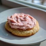 A single Copycat Crumbl Sugar Cookie with a thick layer of bright pink frosting on a white plate.