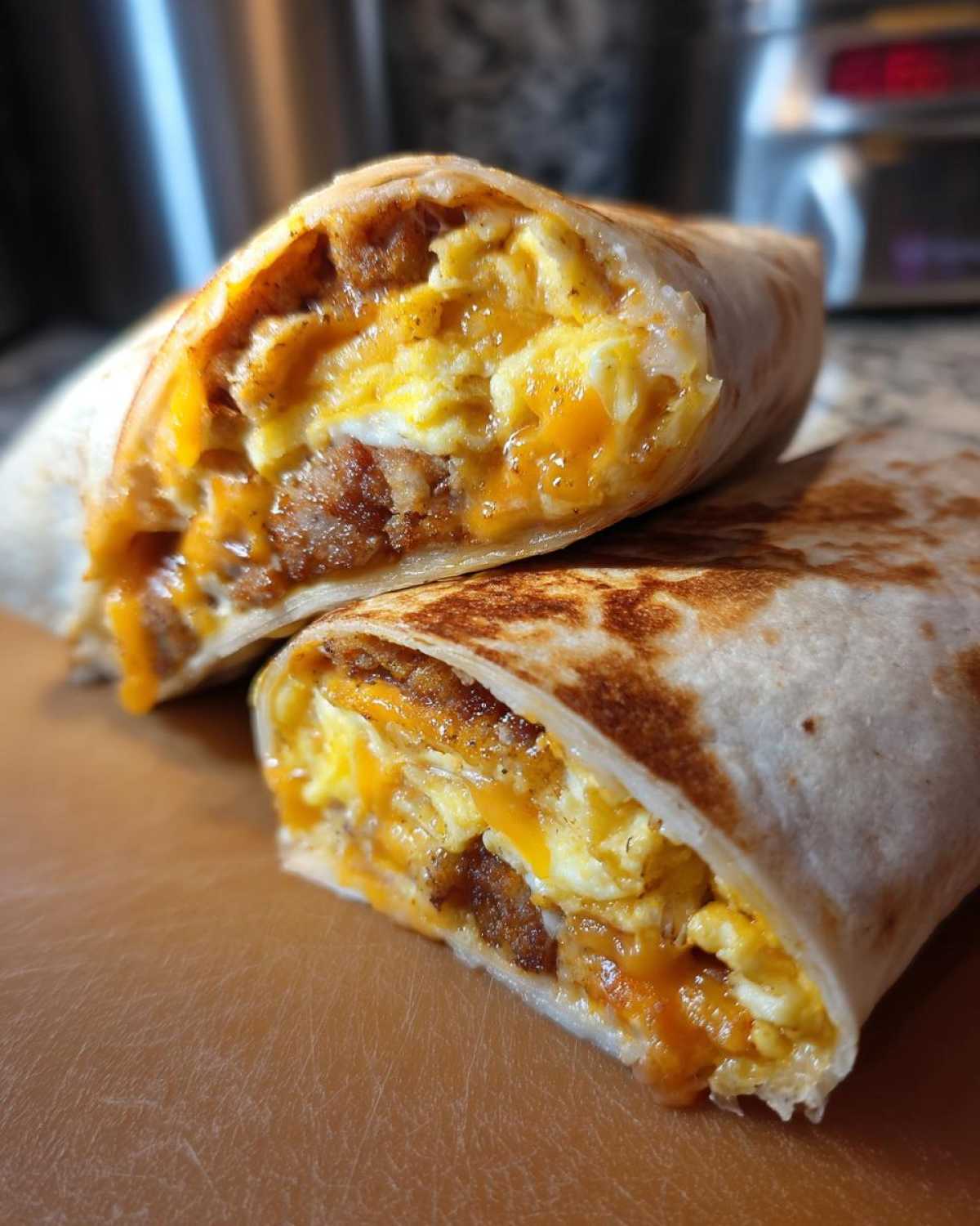 Close-up of a Copycat Dunkin' Wake-Up Wrap cut in half showing scrambled eggs, sausage, and melted cheddar cheese.