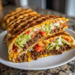 A halved Copycat Taco Bell Crunchwrap Supreme showing layers of seasoned beef, cheese, lettuce, and tomatoes inside a grilled tortilla.