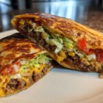 A Copycat Taco Bell Crunchwrap Supreme cut in half showing seasoned beef, lettuce, tomatoes, and melted cheese.