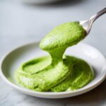 A spoonful of thick, vibrant green Creamy Avocado Cilantro Sauce being lifted from a white bowl.