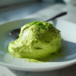 A scoop of bright green, thick Creamy Avocado Cilantro Sauce garnished with finely chopped herbs on a white plate.