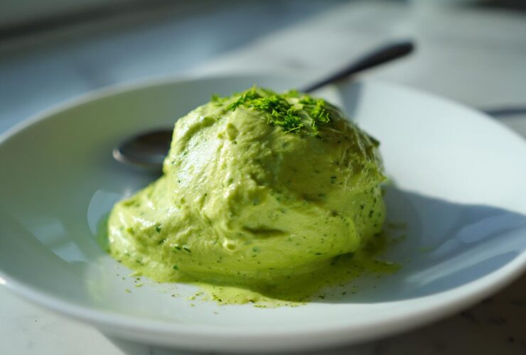 A scoop of bright green, thick Creamy Avocado Cilantro Sauce garnished with finely chopped herbs on a white plate.