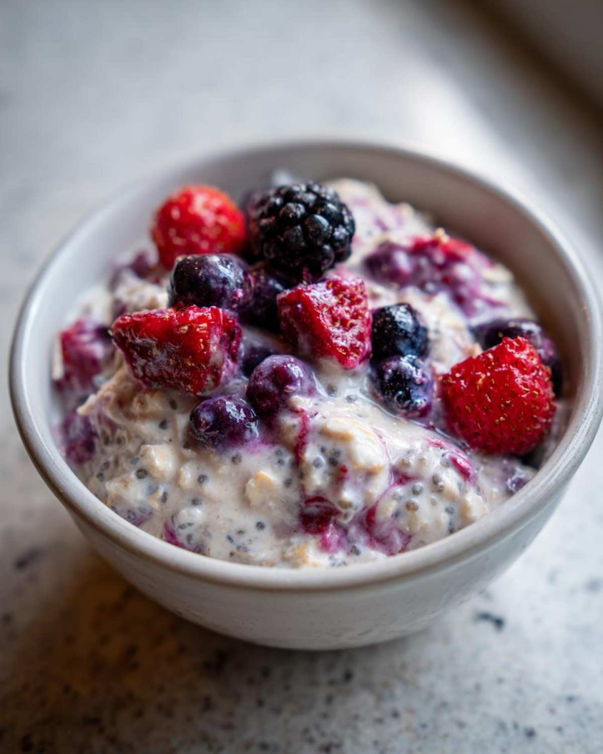 A close-up of Easy Berry Chia Overnight Oats topped with fresh strawberries, blueberries, and blackberries in a white bowl.