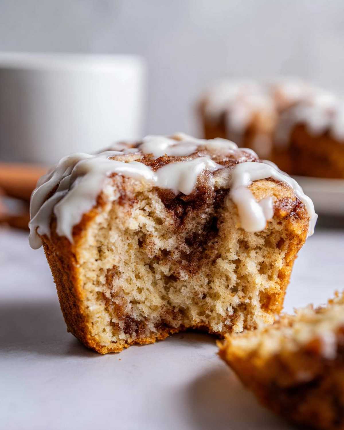 Close-up of a Gluten-Free Cinnamon Roll Muffins with a bite taken out, showing the swirl and white icing.