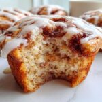 Close-up of a Gluten-Free Cinnamon Roll Muffin with a bite taken out, showing the swirled interior and white glaze.