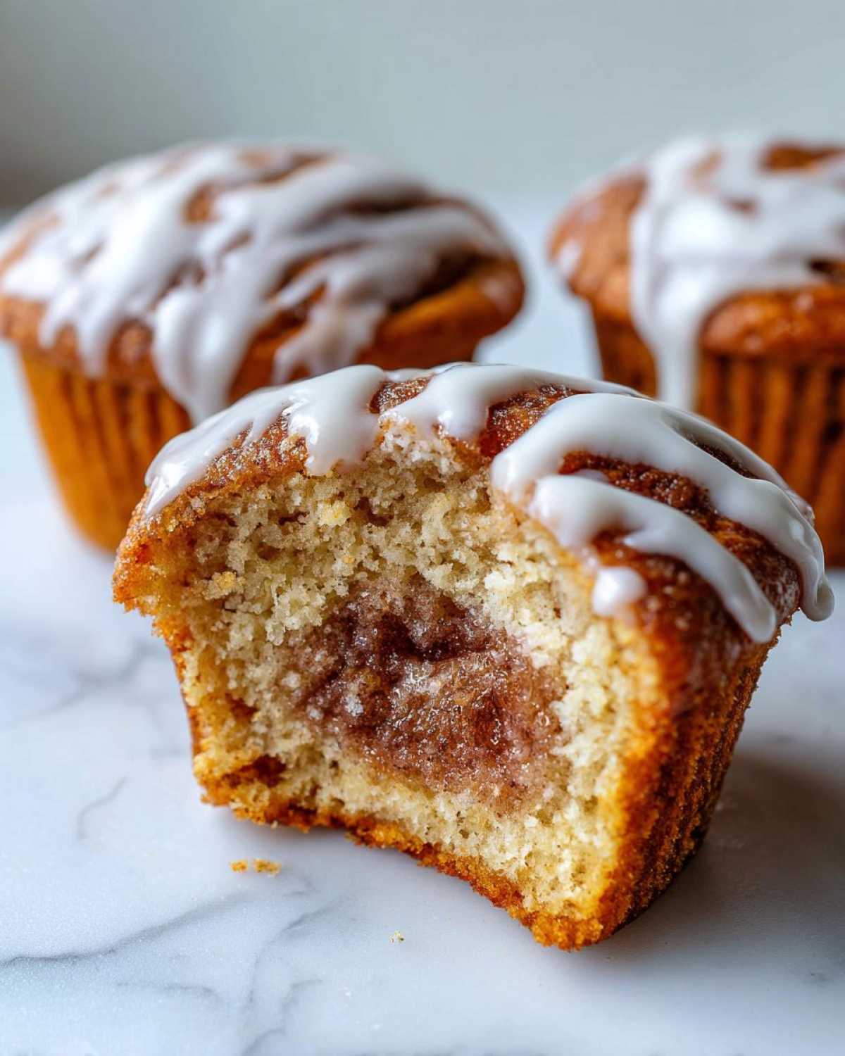 Close-up of a Gluten-Free Cinnamon Roll Muffin cut in half showing the gooey cinnamon swirl center and white glaze.