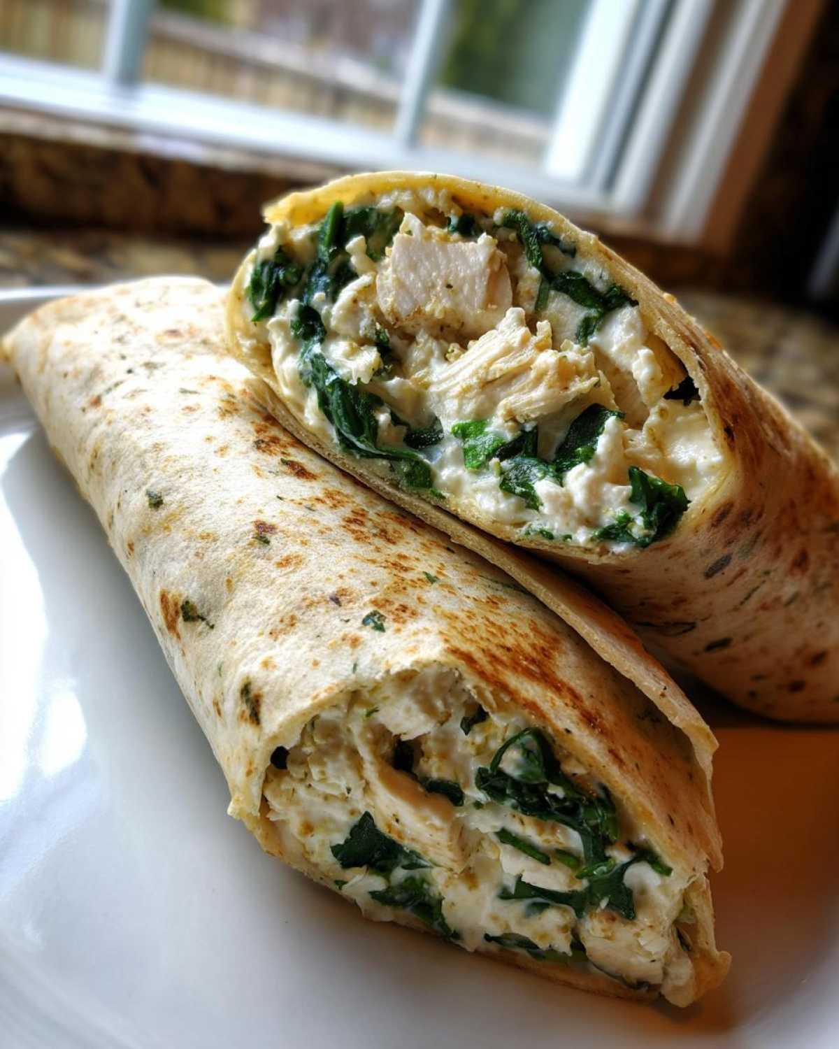 Close-up of a High-Protein Egg White Breakfast Wrap cut in half, showing filling of egg whites, spinach, and chicken.