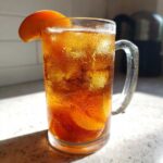 Close-up of condensation-covered glass mug filled with Iced Peach Green Tea, ice, and peach slices.