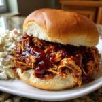 Close-up of a juicy Instant Pot BBQ Pulled Chicken Sandwich piled high with sauce, served with coleslaw.
