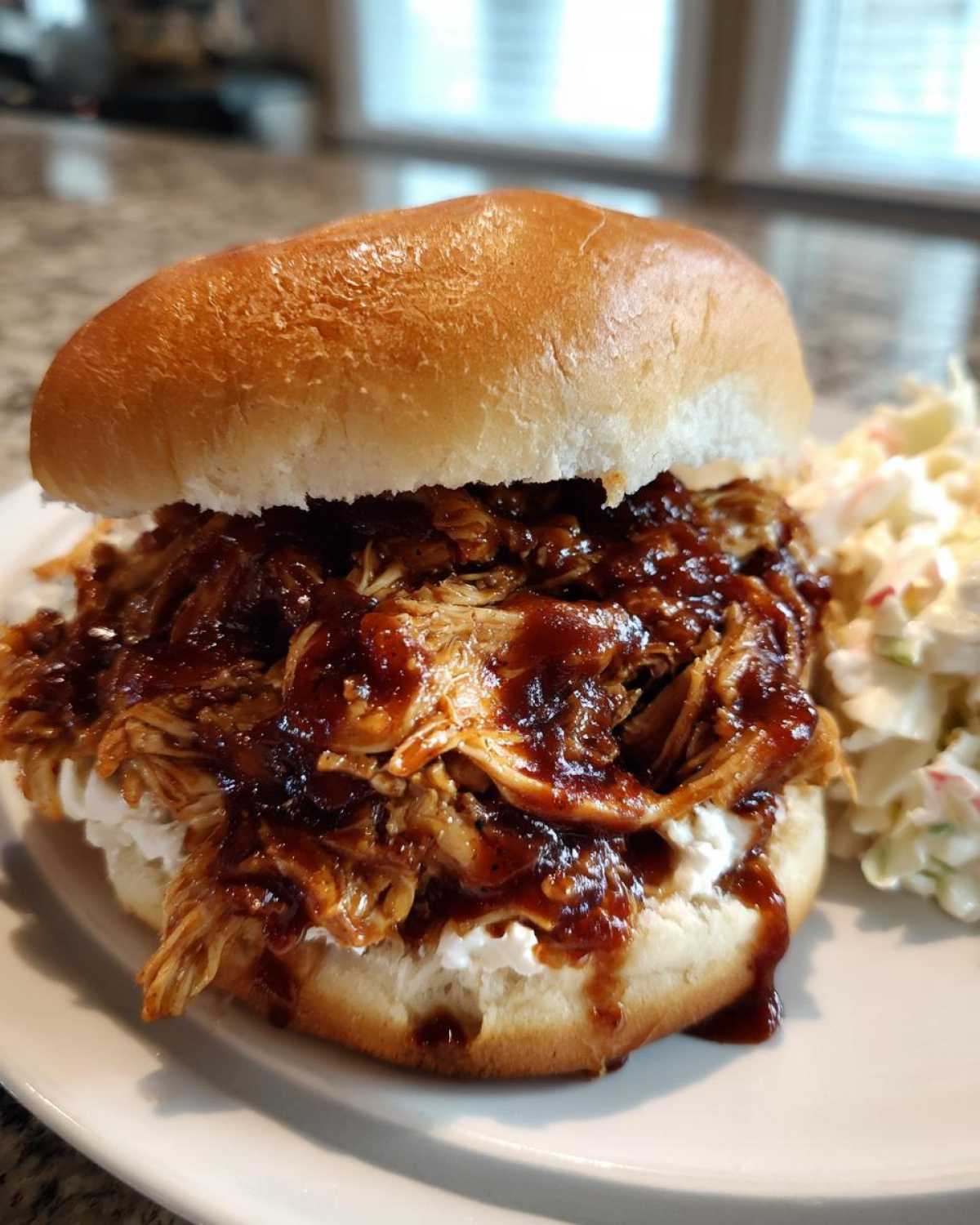 A juicy Instant Pot BBQ Pulled Chicken Sandwich piled high on a bun with creamy coleslaw on the side.