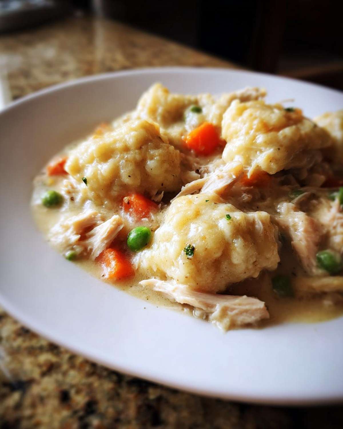 Close-up of fluffy dumplings, shredded chicken, peas, and carrots in creamy sauce for Instant Pot Chicken and Dumplings.