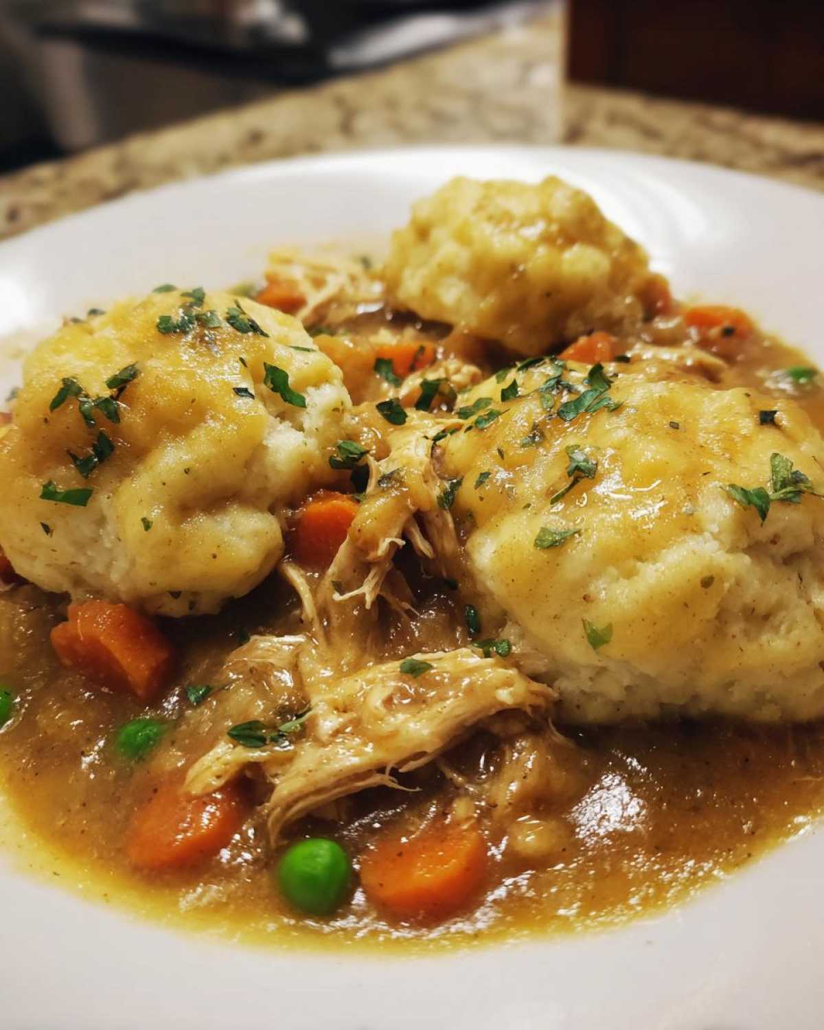 Close-up of a bowl of Instant Pot Chicken and Dumplings with shredded chicken, carrots, peas, and fluffy dumplings.