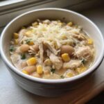 Close-up of a bowl of creamy Instant Pot White Chicken Chili with Corn, topped with shredded cheese.