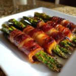 Close-up of perfectly cooked Keto Bacon Wrapped Asparagus Bundles, glistening on a white plate.