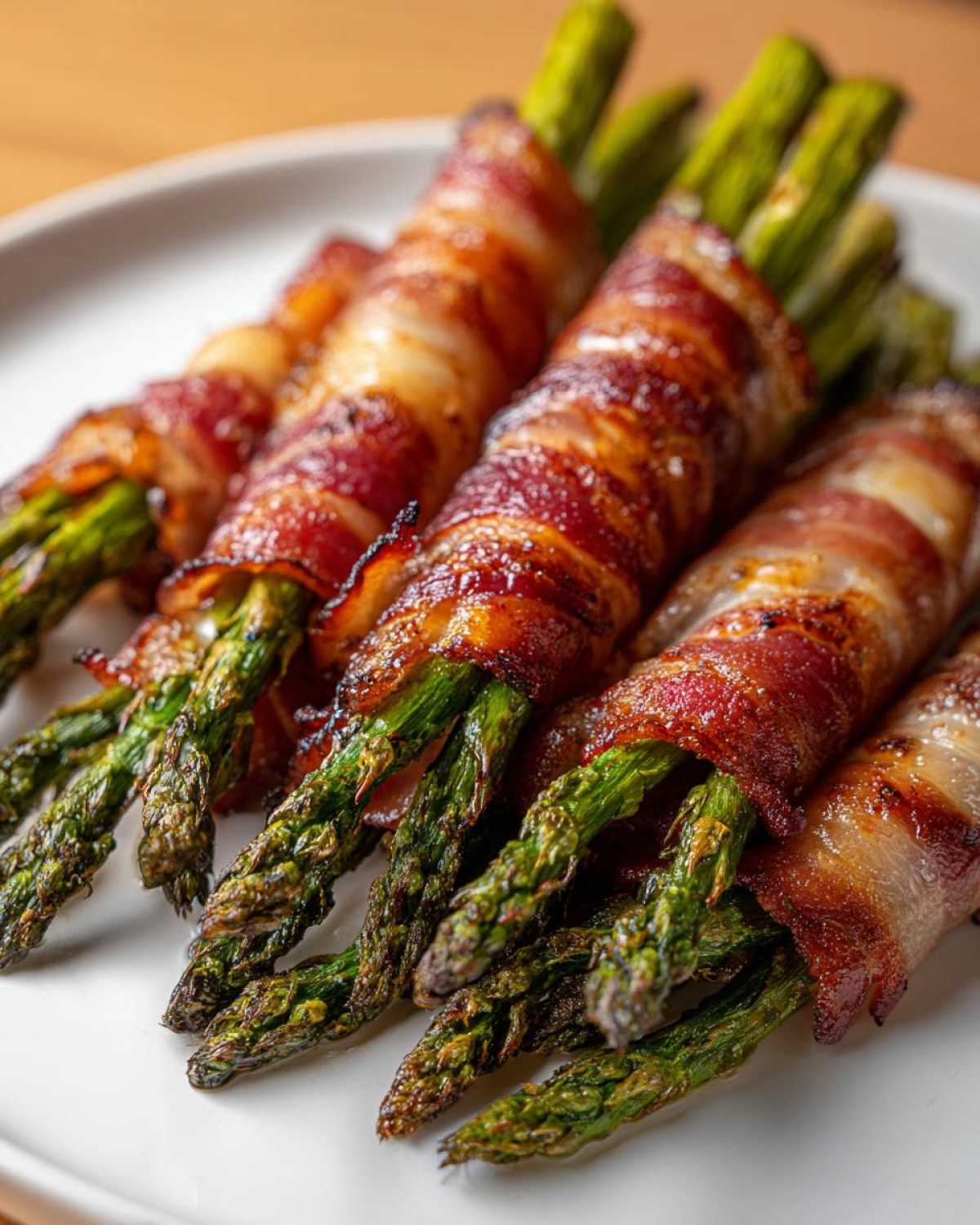 Close-up of perfectly cooked Keto Bacon Wrapped Asparagus Bundles on a white plate.