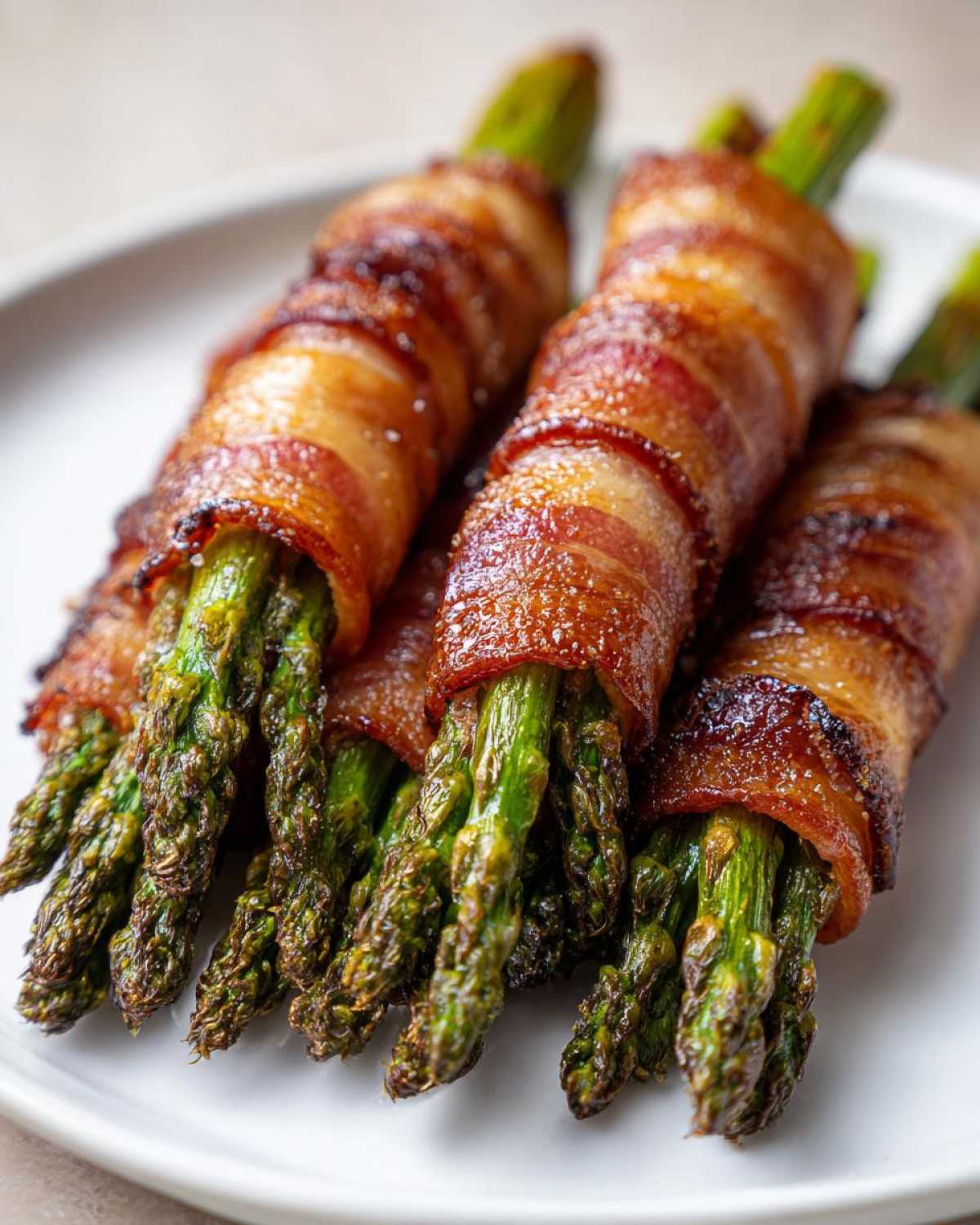 Close-up of perfectly cooked Keto Bacon Wrapped Asparagus Bundles on a white plate.