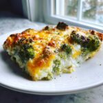 A close-up of a slice of Keto Cheesy Broccoli Casserole with a creamy white base and a golden, bubbly cheese topping.