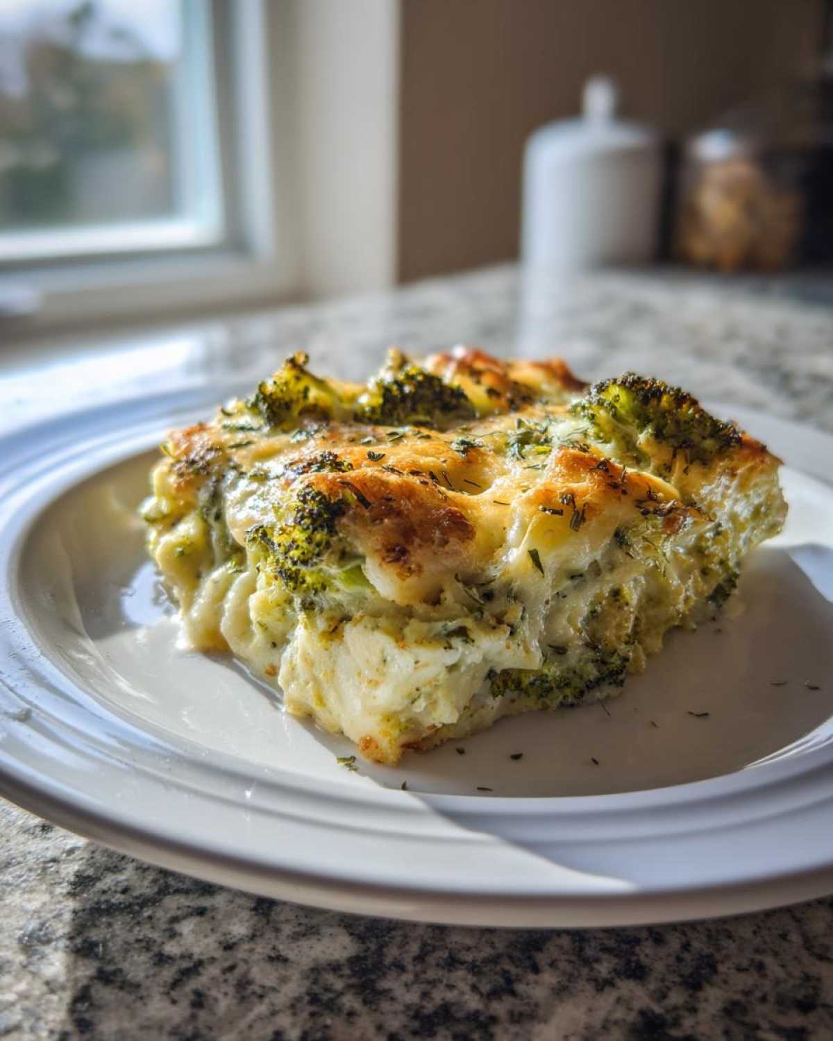 A close-up of a serving of Keto Cheesy Broccoli Casserole on a white plate, featuring melted, browned cheese and visible broccoli florets.