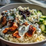 Close-up of Keto Greek Chicken Bowls featuring grilled chicken, cauliflower rice, tzatziki sauce, feta, and cucumbers.