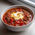 Close-up of a white bowl filled with rich Keto Taco Soup with Ground Beef, topped with sour cream.