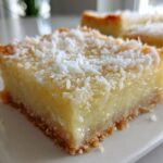 A close-up of a square No-Bake Coconut Lime Bars slice showing the creamy filling and graham cracker crust, topped with shredded coconut.