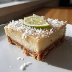 A close-up of a single square of No-Bake Coconut Lime Bars topped with shredded coconut and a lime slice.