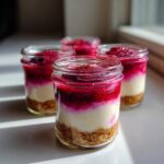 Four individual No-Bake Raspberry White Chocolate Cheesecake Jars showing graham cracker crust, white filling, and raspberry topping.