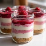 Four layered No-Bake Raspberry White Chocolate Cheesecake Jars topped with fresh raspberries.